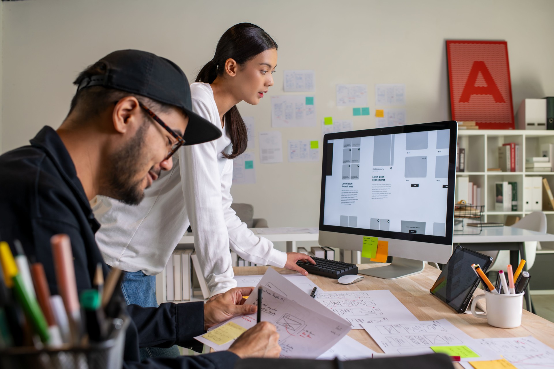 UX UI designers discussing and brainstorming on wireframes for a website and mobile app prototype, surrounded by sketches of user flow and design tools, in the concept of website and mobile application design concept.